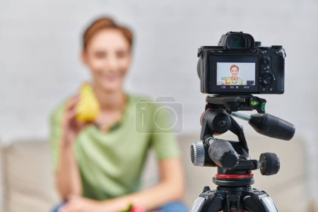 Foto de Enfoque selectivo en la cámara digital cerca de la mujer borrosa con muelle maduro, video blog sobre la dieta a base de plantas - Imagen libre de derechos