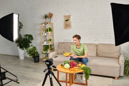 Téléchargez les photos : Femme avec des bananes mûres parlant près de nourriture d'origine végétale fraîche et appareil photo numérique dans le salon vert - en image libre de droit