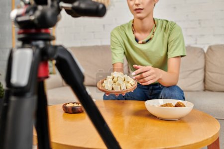 beschnitten Frau zeigt auf Tofu-Käse in der Nähe von pflanzlichen Mehl und Digitalkamera, vegetarische vlog