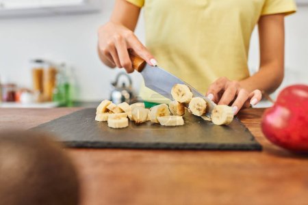 Teilansicht einer jungen Frau, die reife Bananen schneidet, während sie zu Hause in der Küche vegetarisch kocht