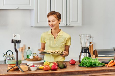 woman with sliced banana on chopping board smiling during vegetarian culinary video blog in kitchen