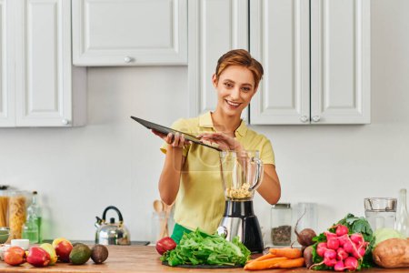 smiley woman with chopping board near electric blender and fresh fruits with vegetables in kitchen
