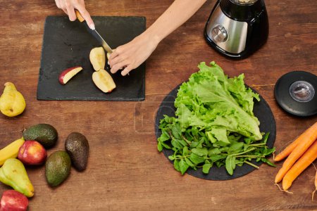 Photo for Cropped view of woman cutting apple near electric blender and lettuce with mint, plant-based diet - Royalty Free Image