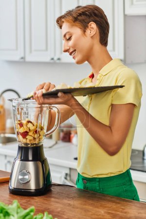 Photo for Woman with cutting board adding chopped fruits into electric blender, wholesome plant-based diet - Royalty Free Image