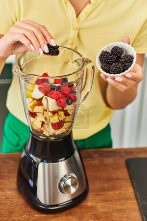 Photo for Cropped view of vegetarian woman adding blackberries into electric blender with delicious fruits - Royalty Free Image