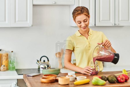 Photo for Pleased woman pouring delicious smoothie from electric blender into mason jar, plant-based diet - Royalty Free Image
