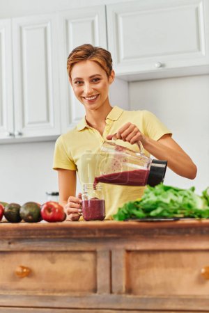 Photo for Vegetarian culinary delight, happy young woman pouring fresh smoothie from blender into mason jar - Royalty Free Image