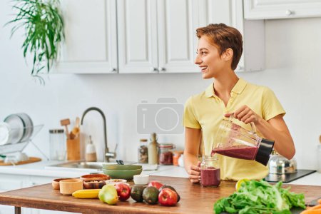 mujer alegre verter batido vegetariano de licuadora en tarro de albañil, concepto de dieta a base de plantas
