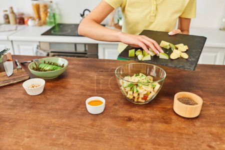 cropped woman holding cutting board with chopped fruits while preparing vegetarian salad at home