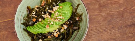 bowl with vegetarian salad with seaweeds and sliced avocado with walnuts on wooden table, banner
