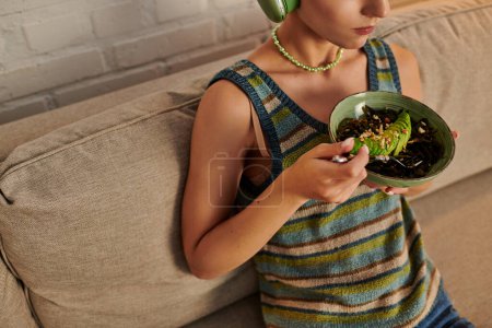 mujer vegetariana recortada sentada con tazón de ensalada con algas marinas y aguacate en rodajas en la sala de estar