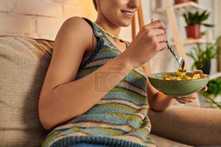 cropped view of smiling woman eating delicious vegetarian salad during dinner in living room