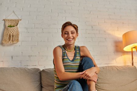 carefree woman looking at camera while sitting on cozy couch in modern living room at home