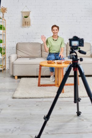 happy young woman waving hand in front of digital camera while starting vegetarian video blog