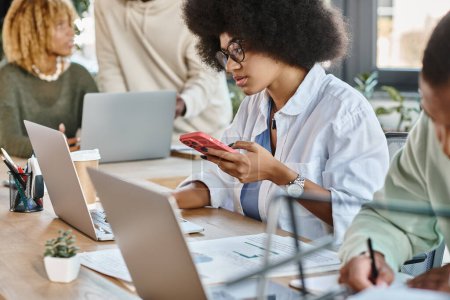 attraktive afrikanisch-amerikanische Frau arbeitet am Laptop mit abgeschnittenem Blick auf ihre Freunde, Coworking