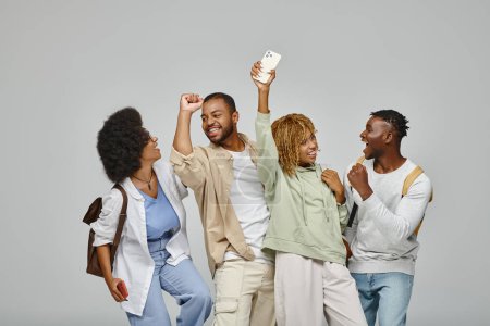 heureux afro-américains étudiants acclamant et souriant joyeusement sur fond gris, étude concept