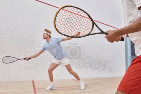 focus on african american man in sportswear playing with redhead friend inside of squash court