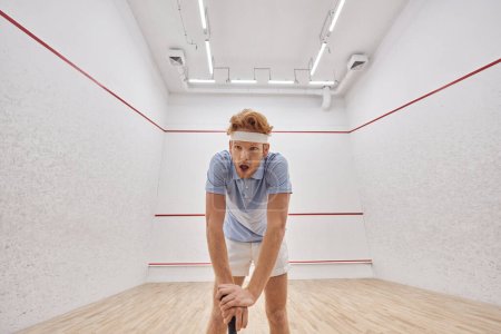 Müder Rotschopf mit Stirnband und Sportkleidung atmet nach Squash-Spiel vor Gericht schwer