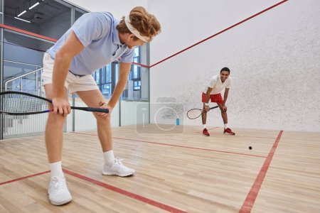 tired interracial friends in sportswear breathing heavily after playing squash in court, motivation