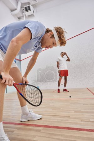 cansados jugadores multiculturales en ropa deportiva respirando pesadamente después de jugar squash en la corte