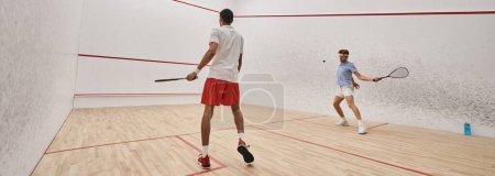 interracial athletic men in sportswear playing squash together inside of court, motivation banner