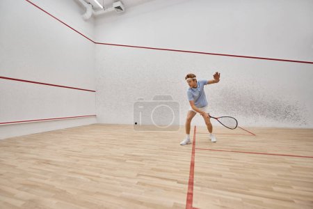 young and active redhead man in sportswear playing squash inside of court, challenge and motivation