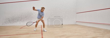 young and active redhead man in sportswear playing squash inside of court, challenge banner