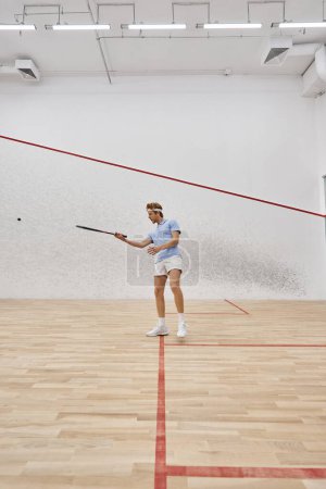 junger rothaariger Sportler mit Stirnband beim Squash auf dem Court, Herausforderung und Motivation