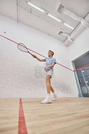 active and redhead player in headband playing squash inside of court, challenge and motivation