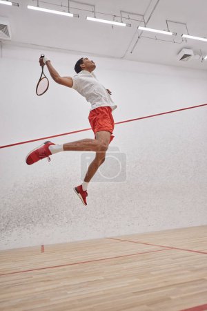 disparo de movimiento, jugador afroamericano motivado sosteniendo raqueta mientras salta y juega squash