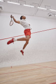 motion shot, motivated african american player holding racquet while jumping and playing squash magic mug #679434248