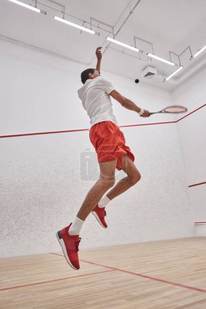 motion photo, active african american sportsman with racquet jumping and playing squash in court