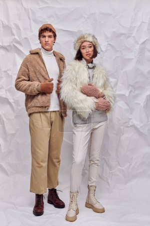 interracial fashion models in cold-weather clothes looking at camera on white textured backdrop