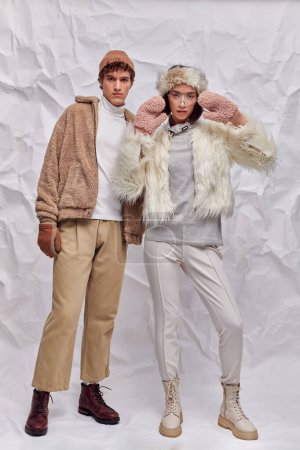 full length of fashionably dressed interracial couple on white crumpled backdrop, winter style