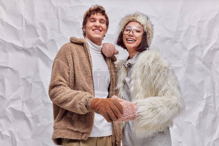 pareja multiétnica de moda en ropa de invierno con estilo sonriendo a la cámara en el fondo de textura blanca