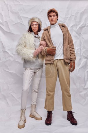 Photo for Young interracial couple in cold-weather attire standing on white textured backdrop, winter styling - Royalty Free Image