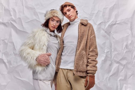 Mode Lookbook-Konzept, interrassische Models in Winterkleidung posieren auf weißem strukturiertem Hintergrund
