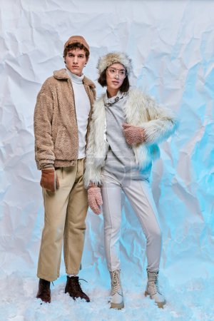 full length of interracial fashion models in cold-weather wear posing on white crumpled backdrop