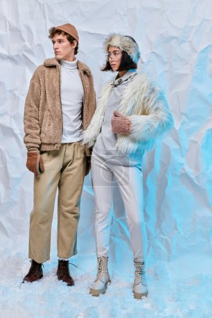 longitud completa de modelos de moda interracial en ropa de clima frío posando sobre fondo blanco arrugado
