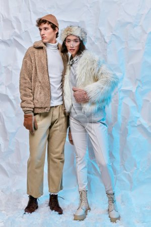 interracial couple in faux fur jackets and boots on white textured backdrop, winter fashion shoot