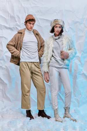 winter fashion lookbook, interracial couple in warm casual attire posing on white snow in studio