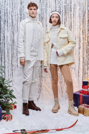 Models blicken in die Kamera neben Weihnachtsbaum und Geschenke auf silbernem Lametta-Hintergrund