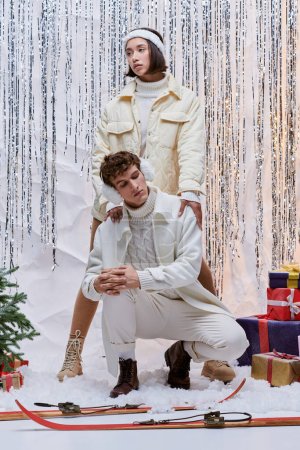 modelos multiétnicos en moda ropa de invierno posando cerca del árbol de Navidad, cajas de regalo y oropel de plata