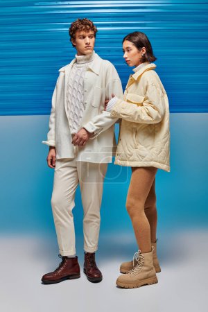 pareja interracial de moda en ropa interior caliente posando sobre fondo azul con lámina de plástico, estilo invierno