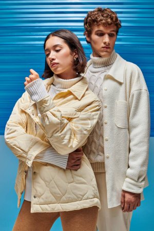pareja interracial vestido de moda en ropa de abrigo sobre fondo de plástico azul, acogedor encanto de invierno