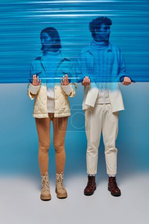 pareja interracial joven en botas de cuero con lámina de plástico azul en el estudio, concepto de estilo de invierno