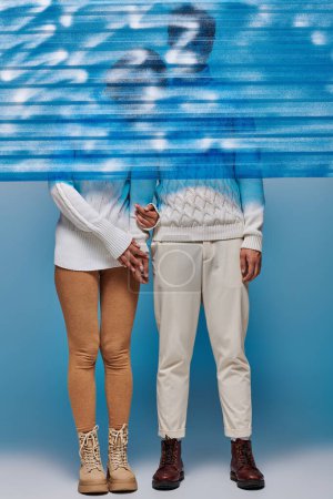 Paar in weißen Pullovern und Lederstiefeln hinter blau gefrorenem Plastik, Wintermode
