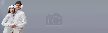 Téléchargez les photos : Ravi couple interracial en pulls chauds posant sur fond gris enneigé, style hiver, bannière - en image libre de droit