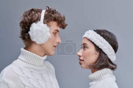 Téléchargez les photos : Vue latérale du couple interracial en chandails blancs et aux cheveux neigeux se regardant sur le gris - en image libre de droit