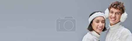 interracial couple in warm outfit smiling gat camera on grey backdrop, urban winter style, banner